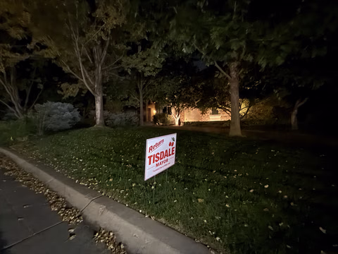 A Doug Tisdale sign on a lawn at night.