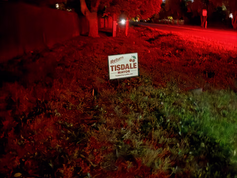 A Doug Tisdale sign beneath trees illuminated by red evening lighting.